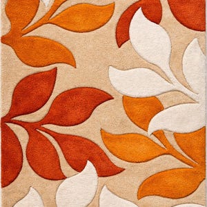 May include: A beige area rug with a repeating leaf pattern in shades of orange and white. The leaves are stylized and arranged across the rug's surface, creating a textured, decorative design. The rug is suitable for living rooms and bedrooms.
