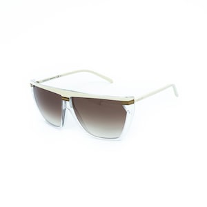 May include: Clear-framed sunglasses with a gradient brown lens. The sunglasses have a white top frame and arms with gold-colored accents. The sunglasses are a modern, stylish accessory.