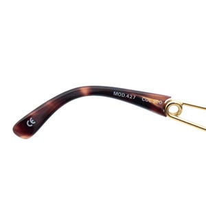 K&ouml;nnte beinhalten: Nahaufnahme des B&uuml;gels einer Brille. Der B&uuml;gel hat ein dunkelbraunes Schildpattmuster mit dem Aufdruck "MOD.427 COL.900". Das Ende des B&uuml;gels hat ein goldfarbenes Metalldetail.