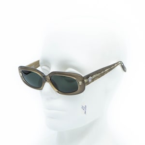 May include: Light brown rectangular sunglasses with dark lenses. The temples feature a textured pattern and a silver emblem near the hinges. The sunglasses are displayed on a white mannequin head.