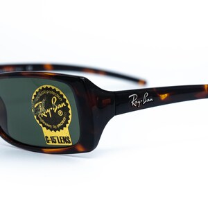 Puede incluir: Gafas de sol Ray-Ban con montura de carey y lentes verdes. Las gafas de sol tienen el logotipo de Ray-Ban en la patilla y una pegatina en la lente que dice "UV protection" y "G-15 LENS".