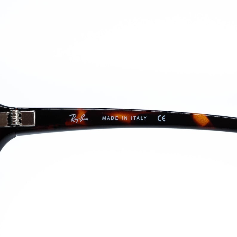 Puede incluir: Primer plano de gafas Ray-Ban con un patr&oacute;n de carey. La montura presenta el logotipo de Ray-Ban y el texto "MADE IN ITALY" y "CE". Las gafas tienen un dise&ntilde;o cl&aacute;sico.