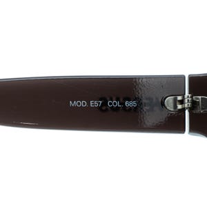 K&ouml;nnte beinhalten: Nahaufnahme einer braunen Sonnenbrille. Der Text "MOD. E57 COL. 685" ist auf dem Rahmen aufgedruckt. Die Sonnenbrille hat ein silbernes Scharnier.