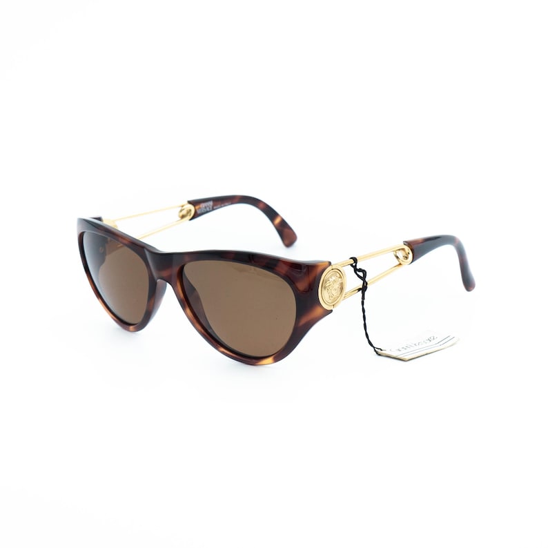 K&ouml;nnte beinhalten: Schildpatt-Sonnenbrille mit braunen Gl&auml;sern. Die Fassungen haben eine Cat-Eye-Form mit goldfarbenen Akzenten an den B&uuml;geln. Die B&uuml;gel sind d&uuml;nn und goldfarben, und die Gl&auml;ser sind ein warmes Braun.