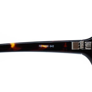 Puede incluir: Primer plano de la patilla de unas gafas. La montura tiene un patr&oacute;n de carey con el texto "RB 4058 642" impreso en blanco. La bisagra es plateada.