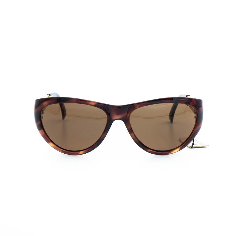 K&ouml;nnte beinhalten: Braune Sonnenbrille mit Schildpattmuster und braunen Gl&auml;sern. Die Sonnenbrille hat ein geschwungenes, umlaufendes Design. Der Rahmen hat ein gesprenkeltes Muster. Die Gl&auml;ser sind einfarbig braun. Die Sonnenbrille ist vor wei&szlig;em Hintergrund platziert.