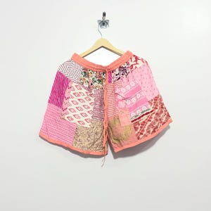 May include: Patchwork shorts featuring a variety of pink, white, and tan fabric patterns including floral, striped, and geometric designs. The shorts have an elasticated waistband with a matching pink drawstring and a finished hem in solid pink.