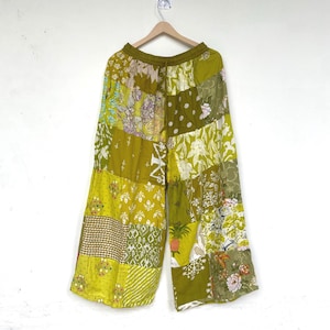 Op de afbeelding: Wijdvallende broek met een patchworkontwerp in diverse tinten olijf-, limoen- en chartreusegroen. Het kledingstuk toont een mix van bloemen-, stippen-, geometrische en botanische patronen, voorzien van een elastische tailleband en een trekkoord.