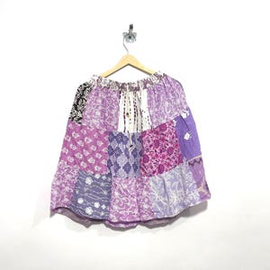 May include: A knee-length skirt featuring a patchwork design in various shades of purple, lavender, and white. The garment has an elasticized waistband with a drawstring closure and is constructed from multiple fabric panels with floral and geometric prints.