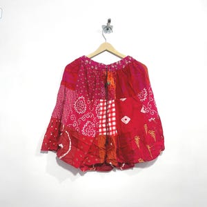 Könnte beinhalten: Ein knielanger Rock mit Patchwork-Design in verschiedenen Rot-, Rosa- und Orangetönen. Das Kleidungsstück besteht aus mehreren Stoffbahnen mit unterschiedlichen Mustern, darunter weiße Blumenmotive, Vichy-Karos und Paisley-Drucke.