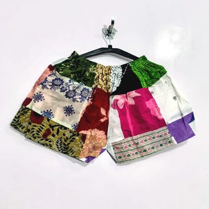 Könnte beinhalten: Eine Shorts mit Patchwork-Design aus verschiedenen Stoffresten. Das Kleidungsstück zeigt eine Mischung aus floralen, geometrischen und einfarbigen Mustern in den Farben Grün, Weiß, Rot, Pink und Lila mit einem elastischen Bund.