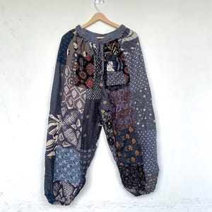 Könnte beinhalten: Patchwork-Hose aus verschiedenen grauen, schwarzen und braunen Stoffbahnen mit unterschiedlichen Mustern wie Blumen-, Punkt- und geometrischen Drucken. Diese weit geschnittene Hose hat einen elastischen Kordelzugbund und schmal zulaufende Beinabschlüsse.
