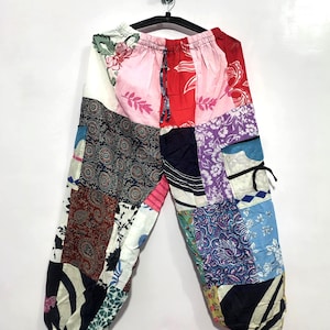Könnte beinhalten: Patchwork-Hose aus verschiedenen bunten Stoffbahnen mit Blumen-, Paisley- und geometrischen Mustern. Die Hose hat einen elastischen Bund mit Kordelzug, Seitentaschen mit schwarzen Bändern und elastische Bündchen an den Beinabschlüssen.