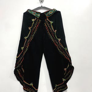 Könnte beinhalten: Schwarze Hose mit weitem Bein und überlappendem Vorderteil. Die Kanten sind mit aufwendigen, bunten Zickzack-Stickereien in Rot, Orange, Grün und Blau verziert und mit einer feinen schwarzen Spitzenborte abgeschlossen.