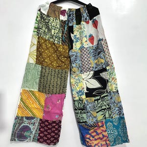 Könnte beinhalten: Weit geschnittene Hose mit einem Patchwork-Design aus verschiedenen Stoffquadraten. Die Muster umfassen florale Drucke, Streifen, geometrische Formen und Erdbeermotive in einer lebendigen Farbpalette aus Gelb, Rosa, Blau, Grün und Schwarz.