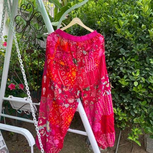 Könnte beinhalten: Weit geschnittene Hose mit einem lebendigen Patchwork-Design in leuchtenden Pink-, Rot- und Orangetönen. Das Kleidungsstück verfügt über einen elastischen Bund und geraffte Beinabschlüsse mit verschiedenen Blumen- und Geometriemustern.