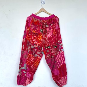 Könnte beinhalten: Weit geschnittene Hose mit einem lebendigen Patchwork-Design in verschiedenen Rot- und Rosatönen. Das Kleidungsstück verfügt über einen elastischen Bund und geraffte Beinabschlüsse an den Knöcheln mit einer Mischung aus Blumen-, geometrischen und Punktmustern.