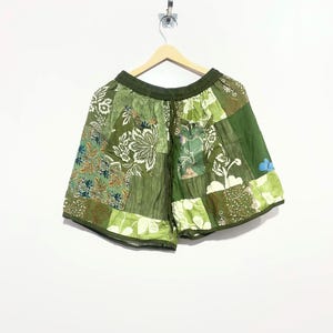 May include: A pair of olive green patchwork shorts featuring an elastic waistband with a drawstring. The garment is constructed from various fabric panels in shades of green, showcasing diverse floral and botanical patterns throughout the design.