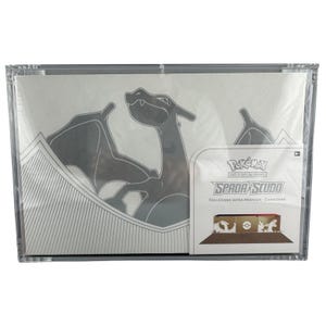Puede incluir: Una caja sellada de la colección Pokémon Ultra Premium. La caja presenta un diseño blanco y gris con una silueta de Charizard. La caja está encerrada en una funda de plástico transparente. El texto "SPADA SCUDO" y "COLLEZIONE ULTRA PREMIUM - CHARIZARD".