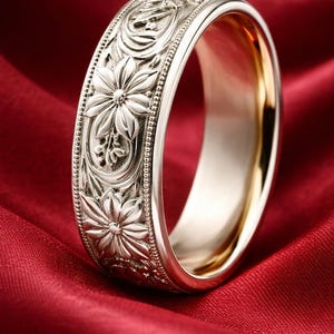 Peut inclure: Une bague en argent avec un motif floral. La bague présente des gravures détaillées de fleurs et de feuilles autour de l'anneau. L'intérieur de la bague est doré, posée sur un satin rouge.