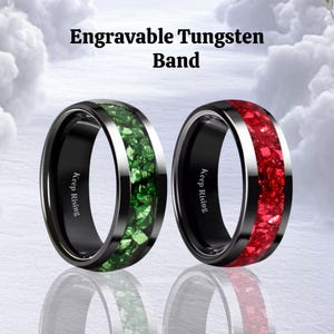 Puede incluir: Se muestran dos anillos de tungsteno con el texto "Keep Rising". Un anillo tiene una banda negra con una incrustación de piedra verde, y el otro tiene una banda negra con una incrustación de piedra roja. El texto "Engravable Tungsten Band" está en la parte superior.