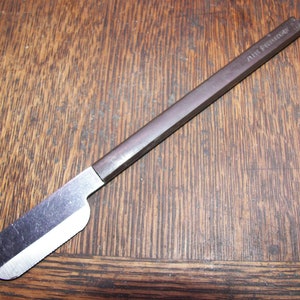 Pode incluir: Uma navalha vintage com cabo castanho escuro e lâmina prateada. A pega tem o texto "AIR FRANCE" gravado. A navalha está sobre uma superfície de madeira.