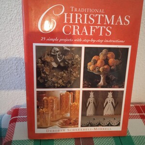 Op de afbeelding: Een boek getiteld "Traditional Christmas Crafts" met een oranje omslag. De omslag toont de titel in het wit en afbeeldingen van verschillende kerstknutselwerken. Het boek bevat 25 eenvoudige projecten met stapsgewijze instructies.