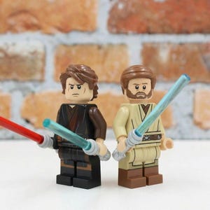 May include: Two Lego figures of characters from Star Wars, one with a red lightsaber and the other with a blue lightsaber. The figures are standing in front of a brick wall.