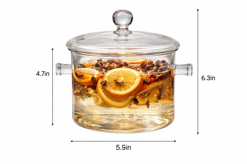 Puede incluir: Una olla de vidrio transparente con tapa, llena de agua, rodajas de naranja y especias. La olla mide 15 cm de ancho y 16 cm de alto, con un asa a cada lado. El contenido parece ser una infusi&oacute;n fragante.