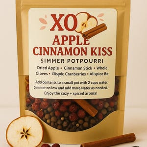 May include: A brown paper bag of "Apple Cinnamon Kiss" simmer potpourri. The label includes text and illustrations of an apple and cinnamon sticks. Ingredients include dried apple, cloves, and cranberries. A sliced apple, cranberries, and spices are displayed.