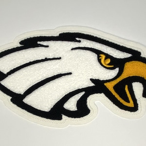 May include: Embroidered eagle head patch with a white body, black outline, and a yellow beak and eye. The patch has a textured, fuzzy appearance and a cream-colored border. This patch is suitable for jackets, bags, or other apparel.