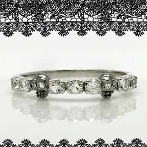 May include: A silver ring with a row of small diamonds and two skull accents.