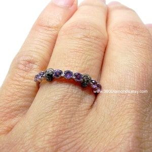 May include: A silver band ring with a skull design and purple gemstones. The ring is on a person's finger.