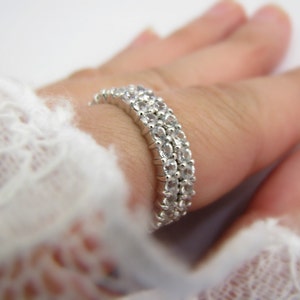 May include: A silver ring with three rows of clear cubic zirconia stones.