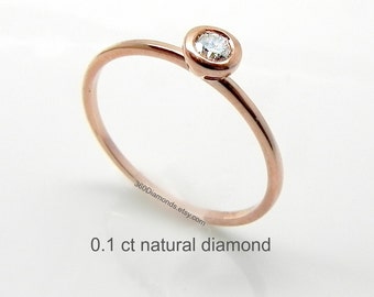 May include: A delicate rose gold ring with a single, round, bezel-set diamond. The diamond is 0.1 carat and is set in a simple, minimalist style. The ring is perfect for everyday wear.