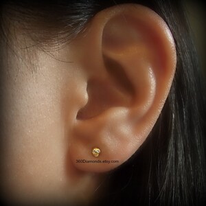 May include: Close-up of a person's ear with a small gold stud earring with a single clear diamond. The earring is in the lobe of the ear.