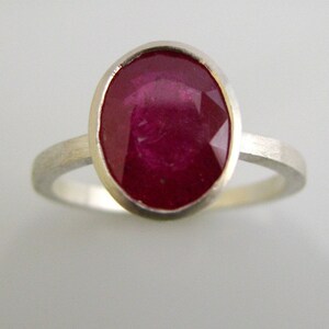K&ouml;nnte beinhalten: Ein silberner Ring mit einem gro&szlig;en, ovalen Rubin-Edelstein, der in einer Zargenfassung gefasst ist.