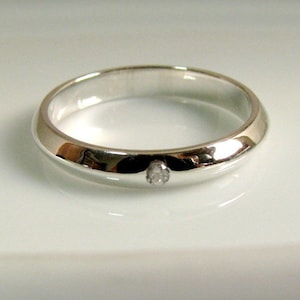 May include: A simple silver band ring with a single small diamond set in the centre.