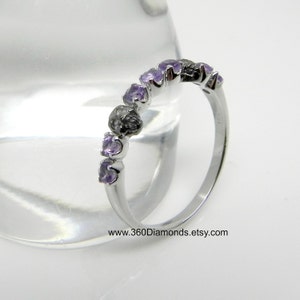 May include: A silver band ring with a row of small, light purple amethyst gemstones set in a curved, prong setting. The ring is on a white background.