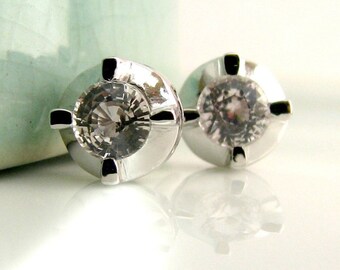 May include: A pair of silver stud earrings with clear round gemstones set in a four-prong setting.