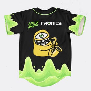 May include: Black baseball jersey with neon green trim and accents. The jersey features the text "Griztronics" above a yellow cartoon character playing a saxophone. A neon green slime design is at the bottom and on the sleeves.