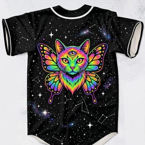 Può includere: Maglia da baseball nera con una grafica vibrante e colorata di un gatto con ali di farfalla e un terzo occhio. Il design presenta uno sfondo di cielo stellato con costellazioni e finiture bianche su maniche e colletto.