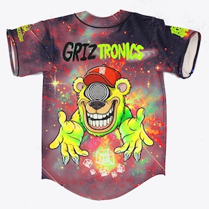 May include: A baseball jersey with a galaxy design. The jersey features the text "Griztronics" in black and neon green, along with a cartoon bear wearing a red cap with a hypnotic eye. The bear has green fur and yellow hands.