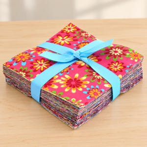 May include: A square stack of fabric squares featuring a vibrant pink background with a repeating pattern of multi-colored flowers in shades of yellow, orange, red, and green. The stack is tied together with a light blue grosgrain ribbon bow.