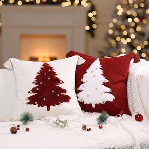 Può includere: Due cuscini decorativi natalizi. Uno è bianco con un design ad albero rosso e l'altro è rosso con un design ad albero bianco. Entrambi i cuscini hanno nappe e sono decorati con piccoli abbellimenti.
