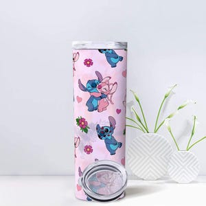 Peut inclure: Un gobelet rose avec un motif r&eacute;p&eacute;t&eacute; de personnages de dessins anim&eacute;s bleus et roses, avec des c&oelig;urs et des fleurs. Le gobelet a un couvercle argent&eacute; et un fond transparent. Le design est fantaisiste et color&eacute;. Le gobelet est de forme cylindrique.