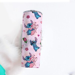 Peut inclure: Un gobelet en acier inoxydable avec un fond rose orn&eacute; d'un motif r&eacute;p&eacute;t&eacute; de personnages de dessins anim&eacute;s bleus et roses, de c&oelig;urs et de fleurs. Les personnages s'embrassent. Le gobelet est cylindrique.