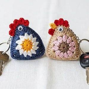 May include: Two handmade crochet chicken keychains. One is navy blue with a white and yellow flower, the other is tan with a pink flower. Both have red combs and googly eyes. Keys are attached.
