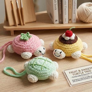Op de afbeelding: Drie handgemaakte gehaakte schildpadbedels in roze, geel en groen, elk met witte accenten. De roze schildpad heeft een groen blad, de gele een kers en de groene een wafelpatroon. Een bord leest "Fruit & Sweets Turtle Trio."
