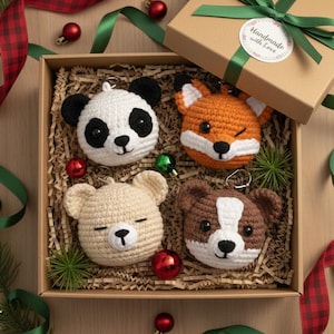 Op de afbeelding: Een geschenkdoos met vier handgemaakte gehaakte dieren sleutelhangers: een panda, een vos, een beer en een hond. De doos is gevuld met houtsnippers en versierd met linten en ornamenten. De geschenkdoos is vastgebonden met een groen lint en een sticker met de tekst "Handmade with Love".